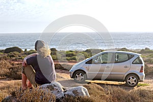Woman dreams while sitting on beach next to her car