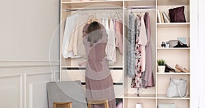 Woman in dress is choosing clothes on a rack in wardrobe searching what to wear.