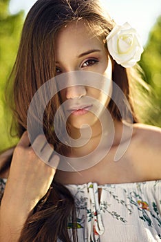 Woman in dress with flower pattern posing with greenery in the background while touching her hair.