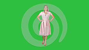 Woman in dress with hands on hips walking while looking at camera on a Green Screen, Chroma Key.