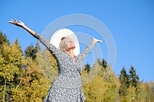 woman in a dress and hat against the background of autumn trees and blue sky on a sunny day