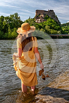 Žena v šatech as vysokými podpatky v ruce při pohledu na starý oravský hrad na Slovensku