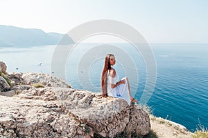 Woman in dress looks at the ocean view from the cliff