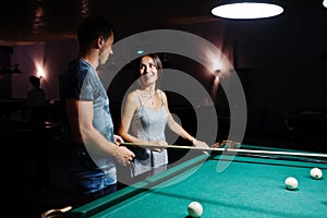Woman in dress playing pool with a man in a pub
