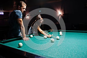 Woman in dress playing pool with a man in a pub