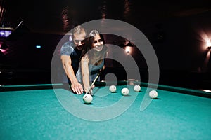 Woman in dress playing pool with a man in a pub