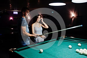 Woman in dress playing pool with a man in a pub