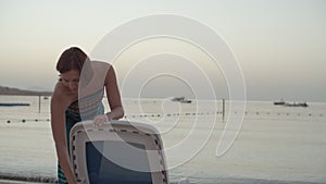 Woman in dress pulling beach chair to the sea. Female taking chaise lounge to the sea and sitting down. Lady relaxing