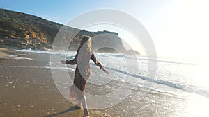 Woman in dress runs along wet beach washed by peaceful ocean