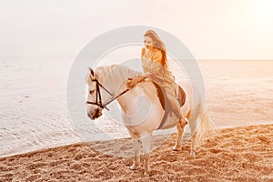 A woman in a dress stands next to a white horse on a beach, with the blue sky and sea in the background.