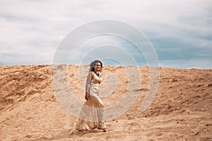 Woman in dress walking in the sand of desert dunes with steps in the desert sand