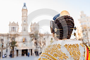 Woman dressed as a Fallera with her back turned, observes the facade of the Valencia City Hall, out of focus in the background