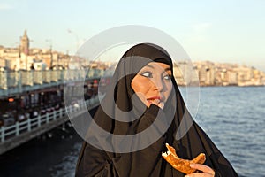 Woman dressed black headscarf, chador eating simit, istanbul, turkey