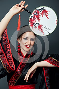 Woman is dressed in red Chinese Japanese folk clothing. Flying fabric, beautiful umbrella and fan in Japanese Chinese style, long