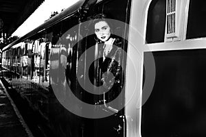 Woman dressed in vintage evening dress leaning out of train window and blowing a kiss