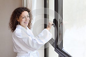 Woman dressed in white bathrobe opens window