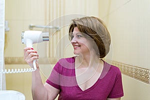 Woman dries hair a hair dryer in a bathroom