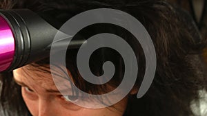 Woman dries her hair with a hairdryer.Brunette with curls, close-up.