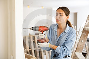 Woman drilling hole in wall with screwdriver in repairable room