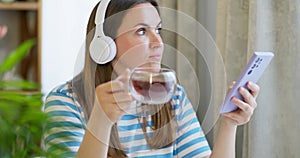 Woman drink a cup of tea and listening to music with headphones in the lounge