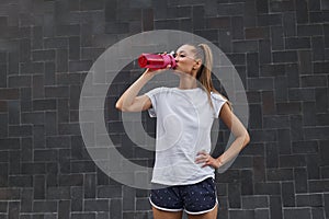 Woman drink water red bottle after morning workout city background