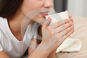 Woman drinking beverage from white ceramic mug indoors, closeup