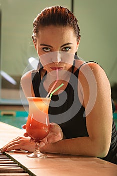 Woman drinking cocktail at swimming pool edge.