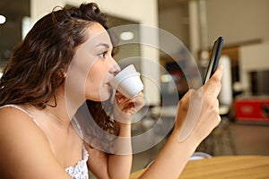 Woman drinking coffee and checking mobile phone in a bar