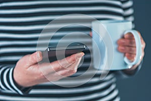 Woman drinking coffee and reading SMS on mobile phone