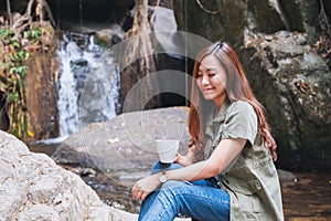 A woman drinking coffee while sitting on the rock in front of waterfall