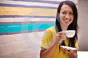 Woman, drinking coffee and smile outdoors, relax and laughing for humor or comedy by wall background. Female person