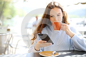 Woman drinking coffee in a terrace checking phone