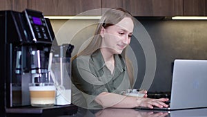 Woman drinking coffee and working on laptop near coffee machine at home.