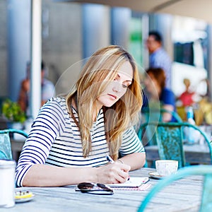 Woman drinking coffee and writing notes in cafe