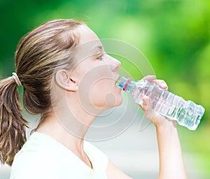 Woman drinking cold mineral water from a bottle after fitness ex