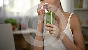 Woman drinking disgusting green smoothie, closing nose, bad smell and taste