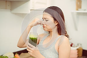 Woman drinking disgusting green smoothie, closing nose, bad smell and taste