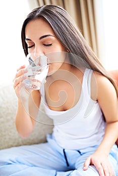 Woman drinking glass of water leaning forward.