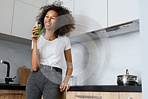 Woman drinking green detox juice, smoothie drink in kitchen