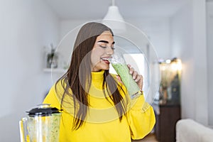 Woman drinking green detox smoothie drink. Happy smiling girl with glass of healthy fresh raw vegetable smoothie at home. Diet