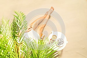 Woman drinking hot coffee with chocolate cookies sitting under palm trees at table. Female on the beach enjoying exotic summer