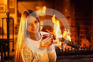 Woman drinking hot coffee relaxing at fireplace.