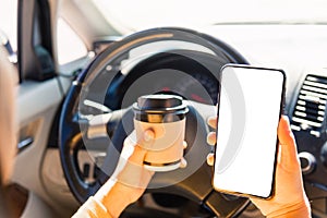 Woman drinking hot coffee takeaway cup inside a car and using smartphone