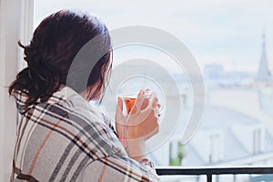 Woman drinking hot tea and looking at the window, cozy winter at home