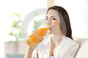 Woman drinking orange juice from a bottle looking at you