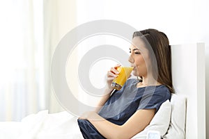 Woman drinking orange juice for breakfast on a bed