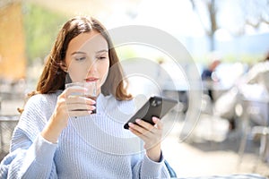 Woman drinking soda in a bar terrace checking phone