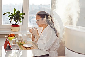 Woman drinking tea reading tablet at humidifier