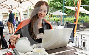 Woman drinking tea and working with laptop on cafe terrace