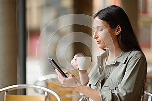 Woman drinking and using smart phone in a terrace